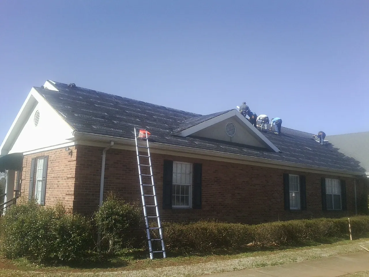 Crew tearing shingles off a brick ranch roof with a ladder set — Emergency Roof Repair work by our crew in Ellerslie