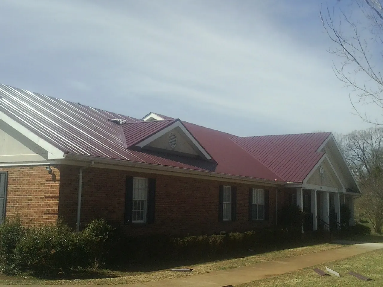 Red metal roof with gabled entries on a long brick building, from a Hail Damage Roof Repair job in Ellerslie
