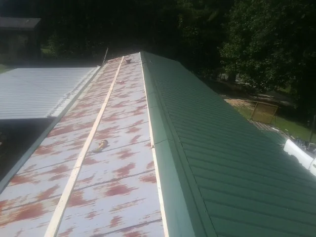 Old rusted panels beside newly installed green metal roofing — Wind Damage Roof Repair by Roofing Brothers in Ellerslie
