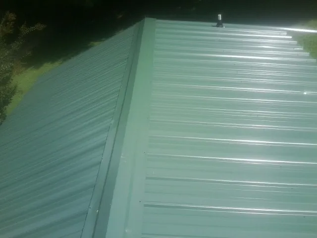 New green metal panels meeting at the ridge of a roof — Flat Roof Repair work by our crew in Ellerslie