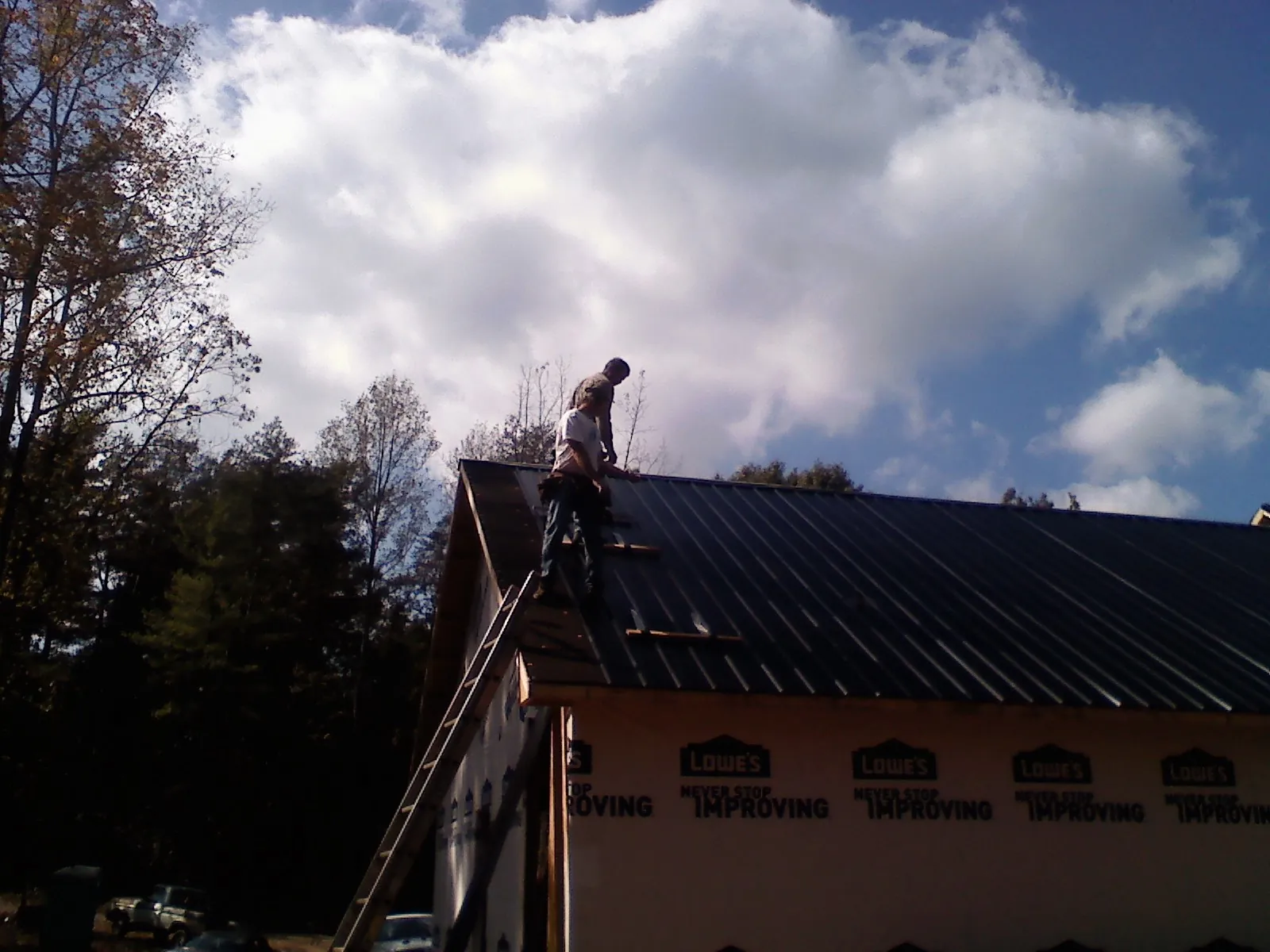 Roofer fastening dark metal panels high against a cloudy sky, from a Roof Inspection job in Ellerslie