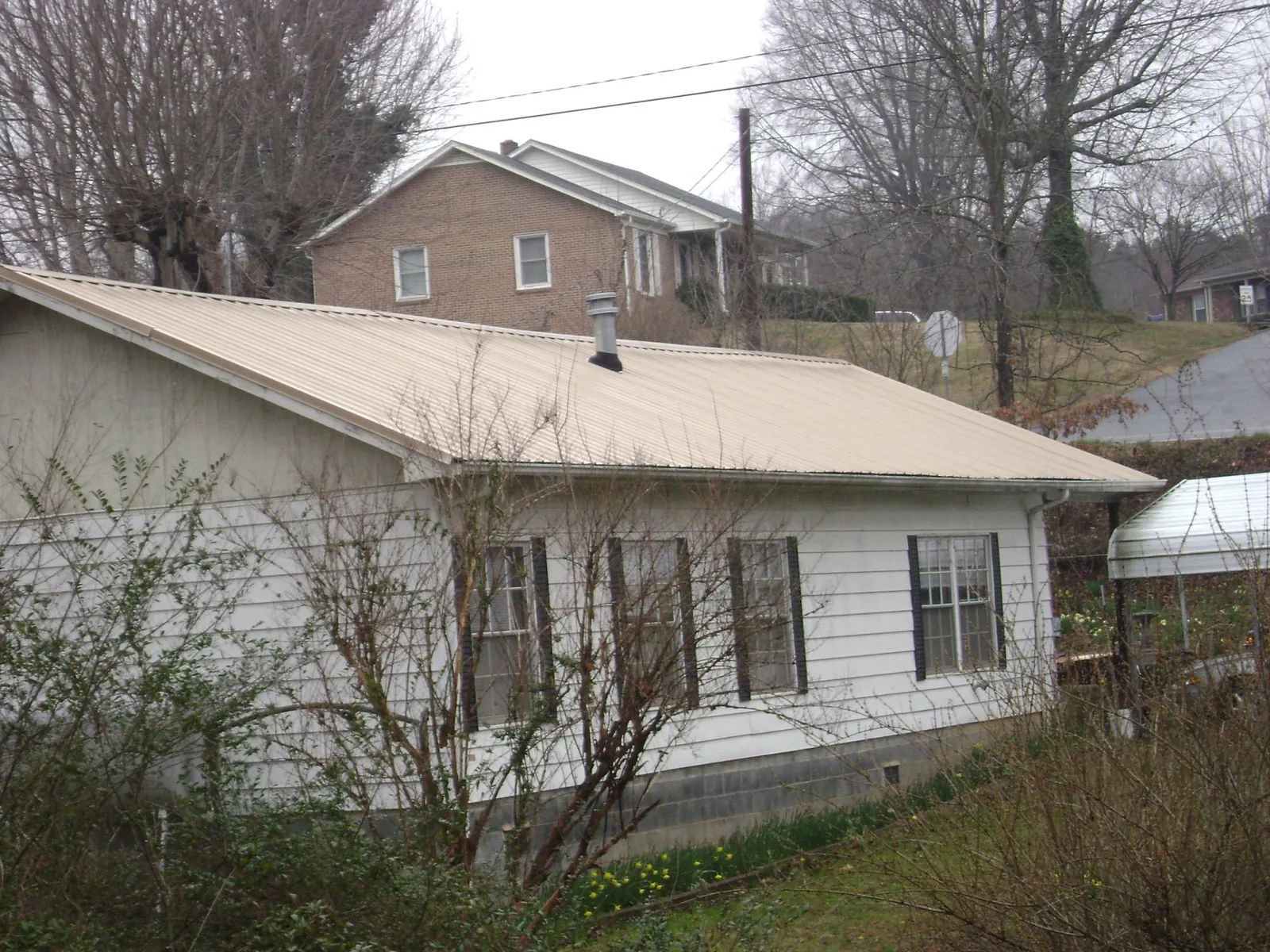 Tan metal roof on a white sided house set into a hillside — Commercial Roofing by Roofing Brothers in Ellerslie